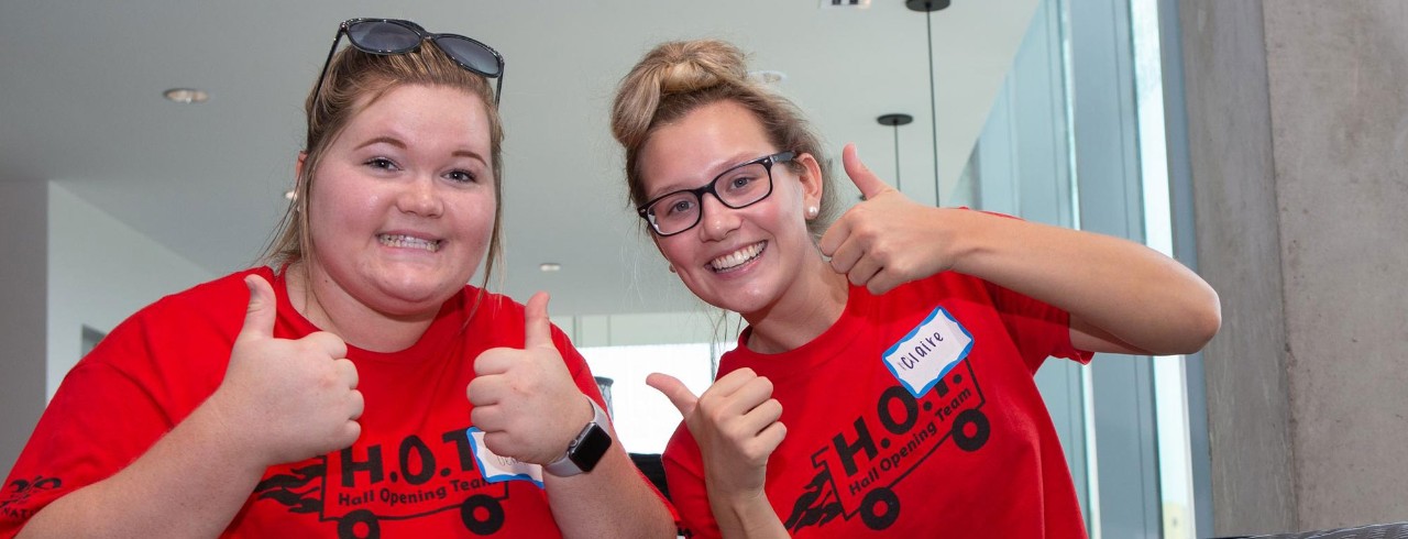 Two females smile and give thumbs up during move in.