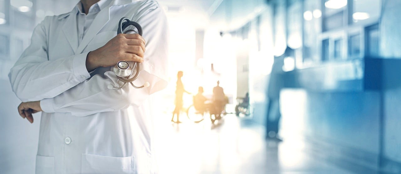 A doctor in a white coat stands in the hallway of a hospital.