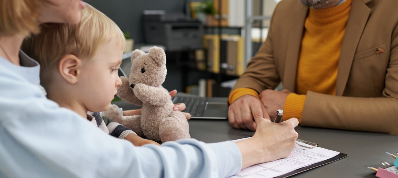 Small child in an adult's lap. Adult is filling out paperwork.